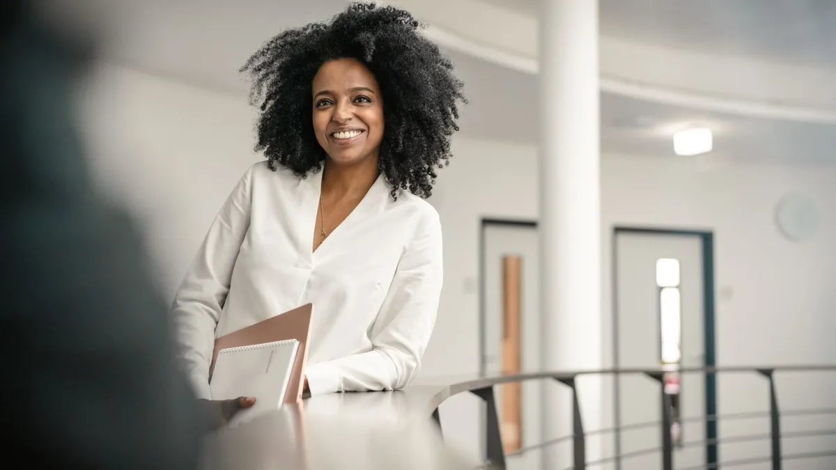 A smiling professional woman holding a folder in an office setting